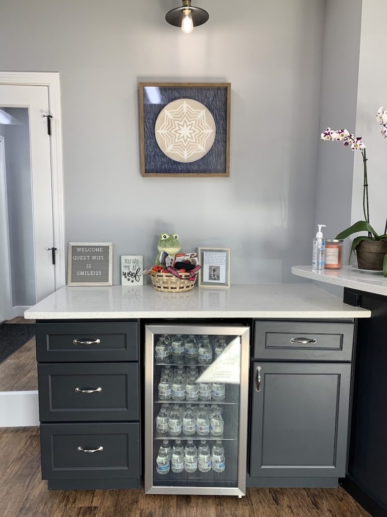 Welcome counter with black drawers and a white marble top, with a water fridge in the middle at Thrive Dental Associates