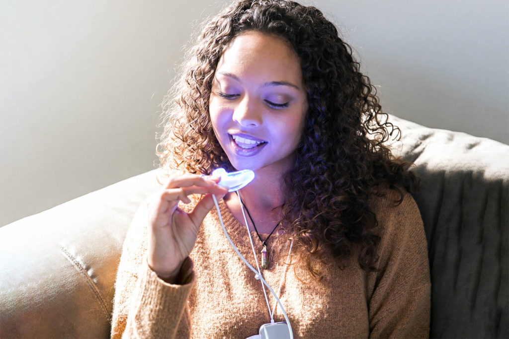 A woman sits in a chair and inserts the GLO at-home teeth whitening tray into her mouth