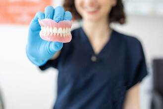 Dental professional holding a full set of dentures at Thrive Dental Associates. Dentures help restore function and appearance for patients with missing teeth.