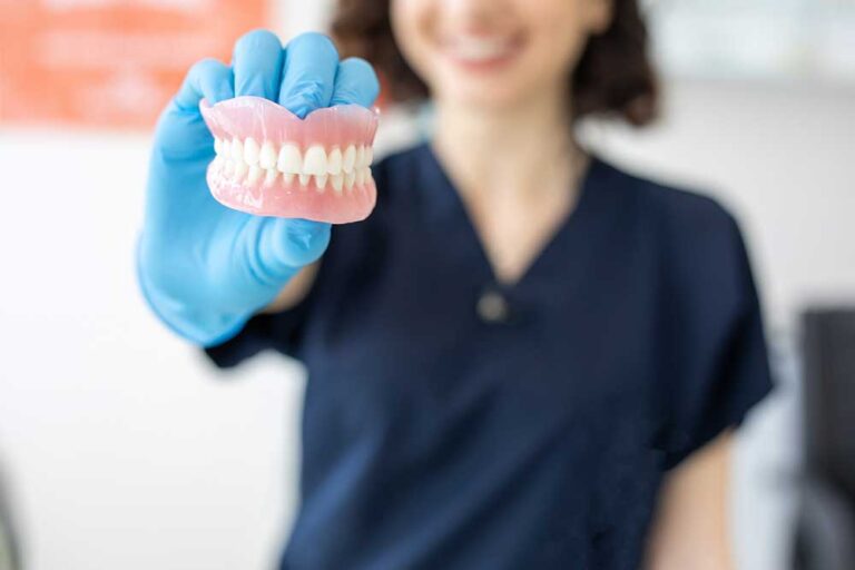 A dental professional in blue gloves holds a close-up model of artificial dentures, showcasing realistic teeth and gum structure for patient education or prosthetic fitting. If you’d like versions tailored for e-commerce, dental clinic branding, or educational content, I can adjust tone and keywords accordingly. Just say the word!
